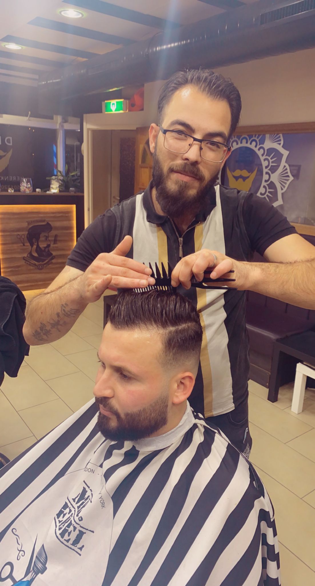 Een kapper van Diva Herenkapsalon knipt met kam en schaar het haar van een klant met baard